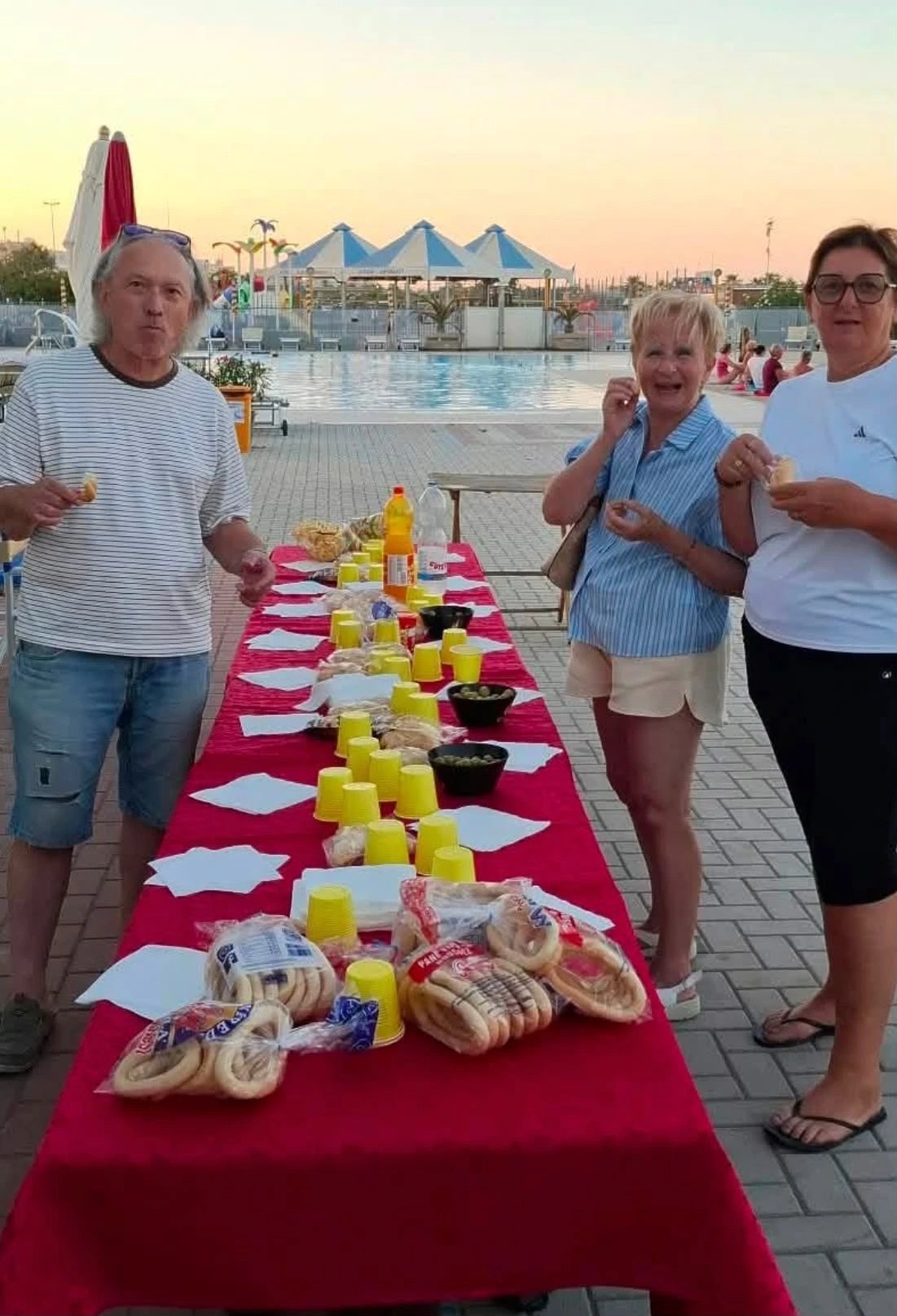 Tavolata con ciambelle, olive e bibite in riva alla piscina, mentre alcuni del gruppo assaggiano